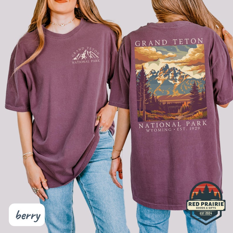 May include: Berry-colored t-shirt featuring the Grand Teton National Park logo on the front and a scenic mountain landscape on the back. The shirt includes the text "Grand Teton National Park Wyoming Est. 1929".