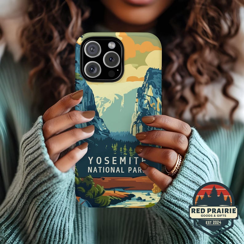 May include: A phone case featuring a scenic illustration of Yosemite National Park. The design includes mountains, trees, and a river, with text that reads "YOSEMITE NATIONAL PAR." The case has a green and yellow top and is held by a person.
