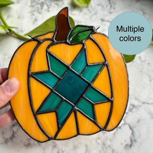 May include: Stained glass pumpkin with a starburst design in shades of orange and teal. The pumpkin has a brown stem and green leaf. The text "Multiple colors" is in a light blue circle.