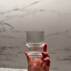 Peut inclure: Un verre en verre transparent avec des crêtes verticales, tenu dans une main. Le verre est vide.