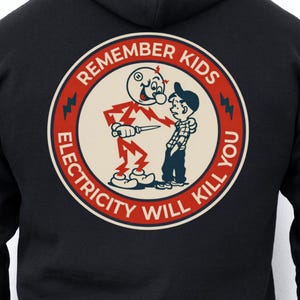 Op de afbeelding: Zwarte hoodie met een cirkelvormige afbeelding op de rug. De afbeelding toont een cartoonfiguur met een mes, een jongen en de tekst "REMEMBER KIDS ELECTRICITY WILL KILL YOU" in een rood-wit ontwerp.