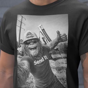 May include: Black t-shirt with a black and white image of a Sasquatch wearing a hard hat and sunglasses, giving a thumbs up. The text "Send It" is printed on the shirt.