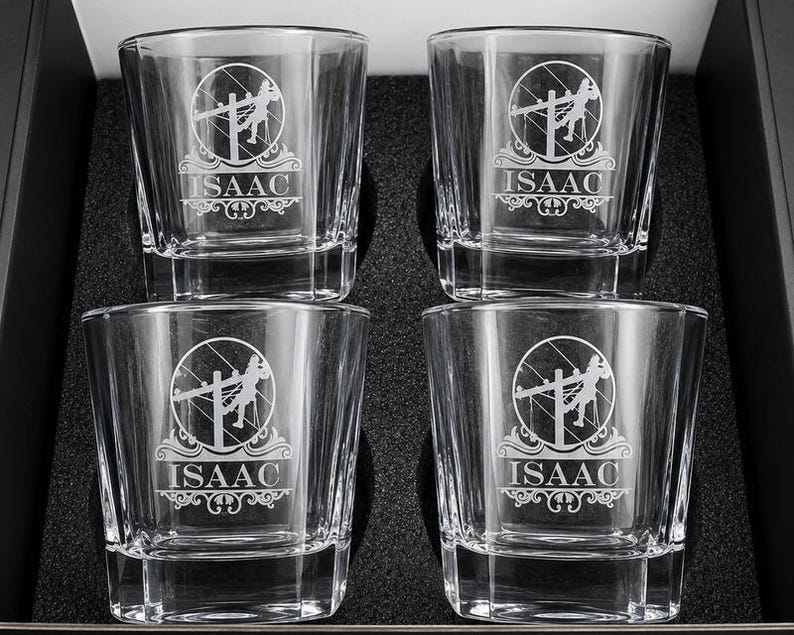 Four personalized Lineman rocks glasses engraved with the name Isaac, arranged in a black foam gift box.
