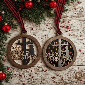 May include: Two wooden Christmas ornaments with a lineman silhouette climbing a utility pole. The ornaments have the words "Merry Christmas" and are surrounded by a circular frame. Red and black plaid ribbon hangs from the top.