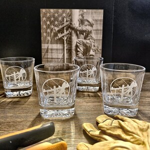 Four rocks glasses engraved with the standard Lineman emblem on a rustic display with lineworker art, tools, and work gloves.