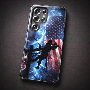 Puede incluir: Funda transparente para teléfono con un diseño que presenta la bandera estadounidense, rayos y una silueta de un liniero en un poste de energía. La funda tiene un acabado brillante y un recorte para múltiples lentes de cámara.