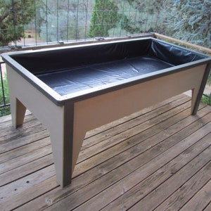 May include: A raised garden bed made of wood with a black plastic liner. The bed is sitting on a wooden deck.