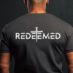 May include: A dark heather grey t-shirt with a white graphic of a cross with nails and the word "REDEEMED" printed on the back.
