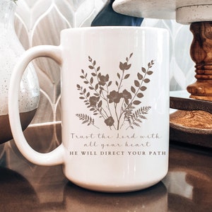 Könnte beinhalten: Weiße Keramiktasse mit Blumenmuster und dem Text "Trust the Lord with all your heart HE WILL DIRECT YOUR PATH".