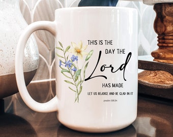 Könnte beinhalten: Eine weiße Keramiktasse mit einem Blumendesign und dem Text "This is the day the Lord has made, let us rejoice and be glad in it."  Psalm 118:24.
