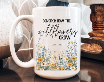 Könnte beinhalten: Weiße Keramiktasse mit einem schwarz-weißen Design mit Wildblumen und dem Text "Betrachte, wie die Wildblumen wachsen" mit dem Bibelvers "Lukas 12:27".