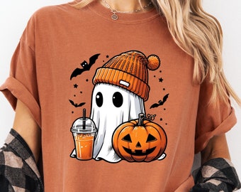 Puede incluir: Camiseta naranja con un diseño de Halloween. Presenta un fantasma de dibujos animados con un gorro naranja, sosteniendo una bebida, con una calabaza y murciélagos.