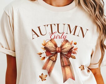 Puede incluir: Camiseta color crema con la inscripción "AUTUMN Girly" sobre un diseño de lazo en acuarela con hojas de otoño. El lazo tiene un estampado de cuadros y está decorado con colores otoñales.