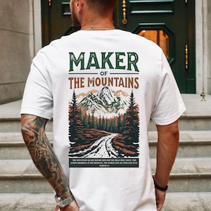 May include: White t-shirt with a graphic of a mountain range and the text "Maker of the Mountains". The text "The mountains stand before Him and the hills melt away. The earth trembles at His presence. The world and all who live in it. Nahum 1:5" is printed below the graphic.