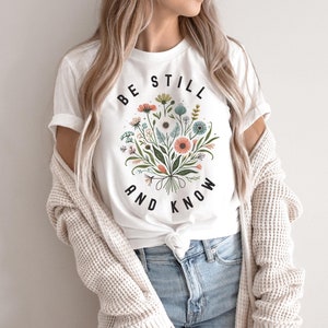 May include: White t-shirt with a floral design and the text "Be Still and Know" in black.