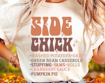 May include: Mustard-colored t-shirt with the text "SIDE CHICK" in brown and pink lettering. Below the text are the words "MASHED POTATOES, GRAVY, GREEN BEAN CASSEROLE, STUFFING, YAMS, ROLLS, CRANBERRY SAUCE, PUMPKIN PIE."