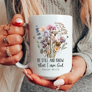 May include: White ceramic mug with a floral design and the text "Be still and know that I am God, Psalm 46:10".