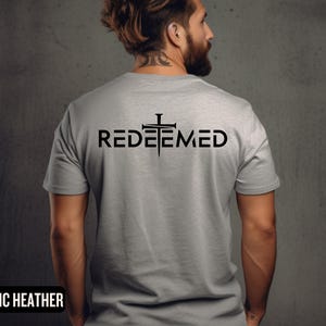 May include: A gray t-shirt with the word "REDEEMED" printed on the back in black lettering. A black cross with nails is above the word.