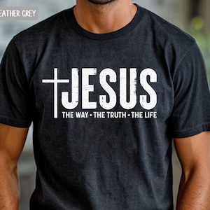 May include: Dark heather grey t-shirt with a white distressed graphic of a cross and the word "JESUS" with the text "THE WAY - THE TRUTH - THE LIFE" underneath.