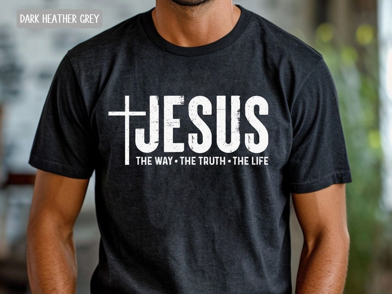 May include: Dark heather grey t-shirt with a white distressed graphic of a cross and the word "JESUS" with the text "THE WAY - THE TRUTH - THE LIFE" underneath.