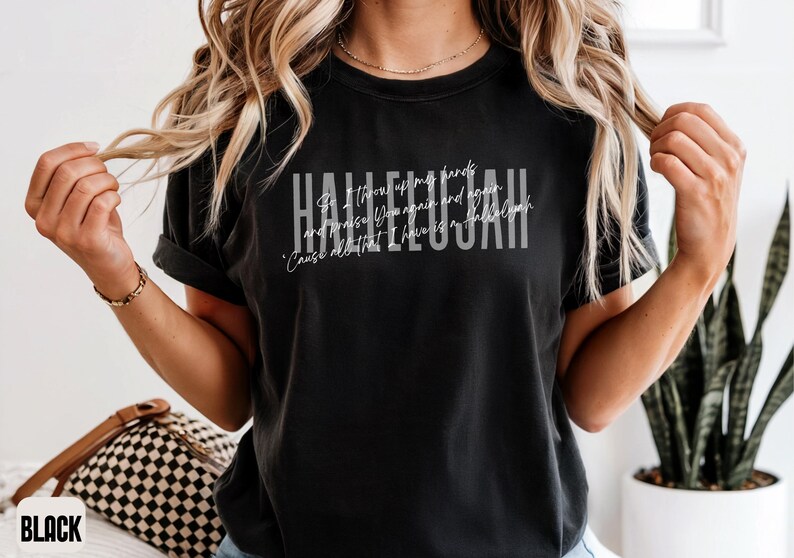 May include: A black short-sleeve t-shirt featuring the word HALLELUJAH in large white block letters. Overlaid in a thin white script font is the text: So I throw up my hands and praise You again and again. 'Cause all that I have is a Hallelujah.