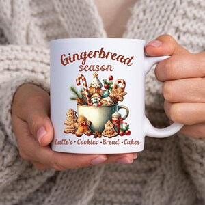 May include: White ceramic mug with a festive "Gingerbread season" design. The mug features a watercolor illustration of gingerbread cookies, candy canes, and a cup filled with treats. Text at the bottom reads "Latte's Cookies Bread Cakes."