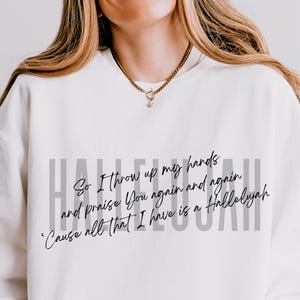 May include: A white crewneck sweatshirt featuring the word HALLELUJAH in large gray capital letters. Overlaid in black cursive script is the text: So I throw up my hands and praise You again and again 'Cause all that I have is a Hallelujah.