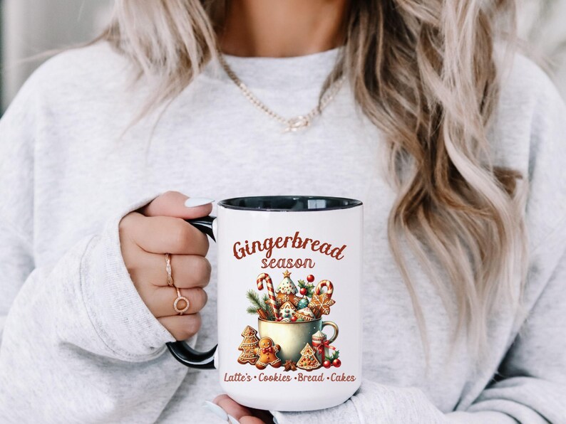 May include: White ceramic mug with a black interior and handle, featuring a "Gingerbread Season" design. The design includes gingerbread cookies, candy canes, and other festive elements. The mug also lists "Latte's &bull; Cookies &bull; Bread &bull; Cakes".