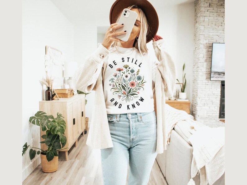 May include: White t-shirt with a floral design and the text "Be Still and Know" printed on the front.