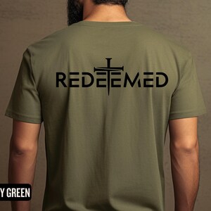 May include: A military green t-shirt with a black graphic of a cross with nails and the word "REDEEMED" underneath.