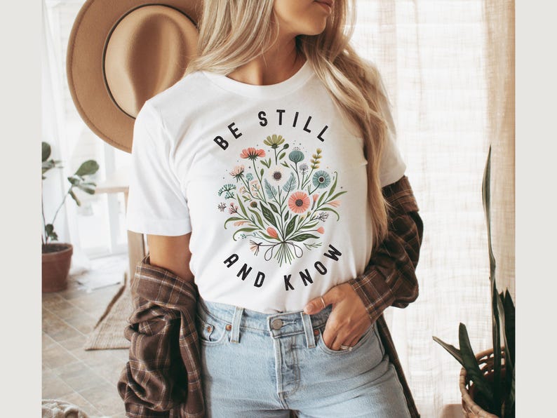 May include: White t-shirt with a floral bouquet graphic and the text "Be Still and Know" in black.