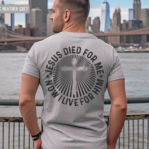 May include: A heather grey t-shirt with a circular design on the back. The design features a cross with radiating lines and the text "JESUS DIED FOR ME * NOW I LIVE FOR HIM".