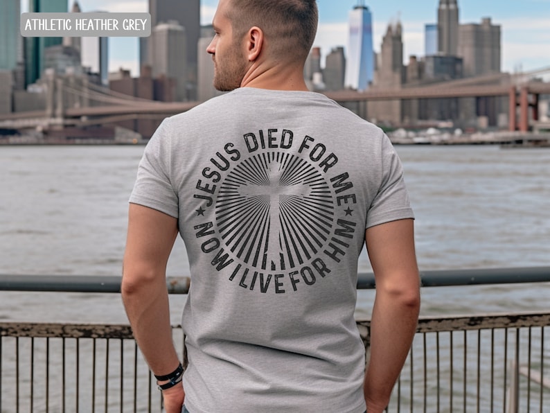 May include: A heather grey t-shirt with a circular design on the back. The design features a cross with radiating lines and the text "JESUS DIED FOR ME * NOW I LIVE FOR HIM".