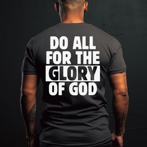 May include: A dark gray t-shirt with the text "Do All For The Glory Of God" printed in white on the back.