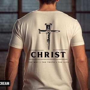 May include: A soft cream colored t-shirt with a black graphic of a nail hammered into a cross shape. The text "CHRIST" is below the graphic with the words "THE WAY | THE TRUTH | THE LIFE" underneath.