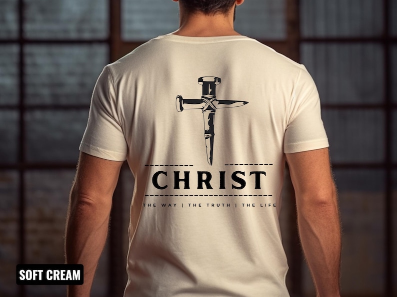 May include: A soft cream colored t-shirt with a black graphic of a nail hammered into a cross shape. The text "CHRIST" is below the graphic with the words "THE WAY | THE TRUTH | THE LIFE" underneath.