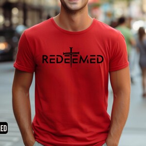May include: A red t-shirt with a black cross and the word "REDEEMED" printed on the front.
