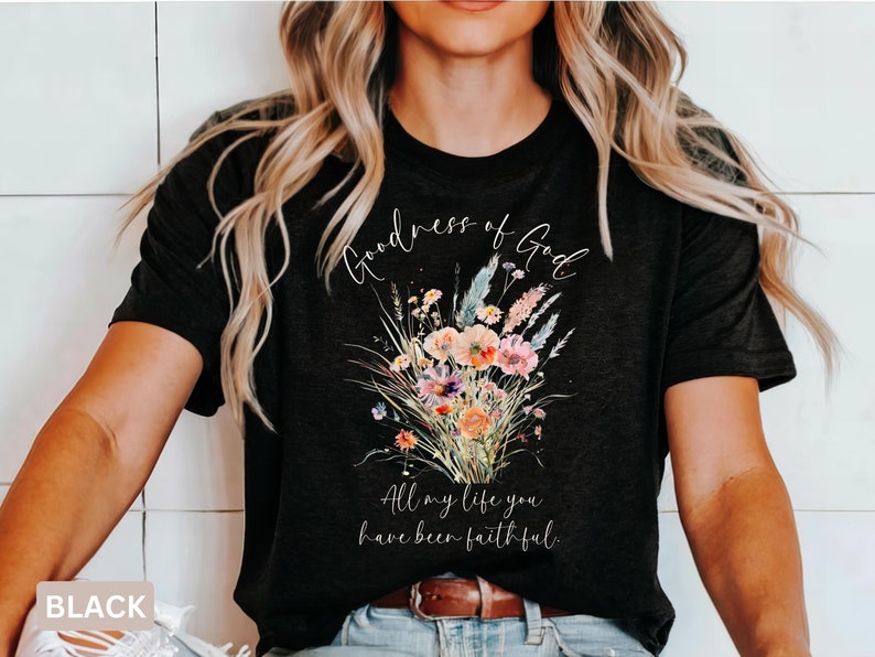 May include: Black t-shirt featuring a floral bouquet design with the words "Goodness of God" and "All my life you have been faithful" in white script. The bouquet includes pink, orange, and blue flowers.