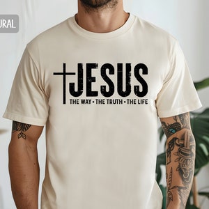 May include: A beige t-shirt with a black graphic that says "JESUS THE WAY - THE TRUTH - THE LIFE" with a cross before the word "JESUS".