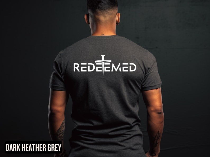 May include: A dark heather grey t-shirt with a white graphic of a cross with nails and the word "REDEEMED" printed on the back.