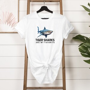 May include: White t-shirt with a blue tiger shark graphic and the text "Tiger Sharks Are My Favorite".