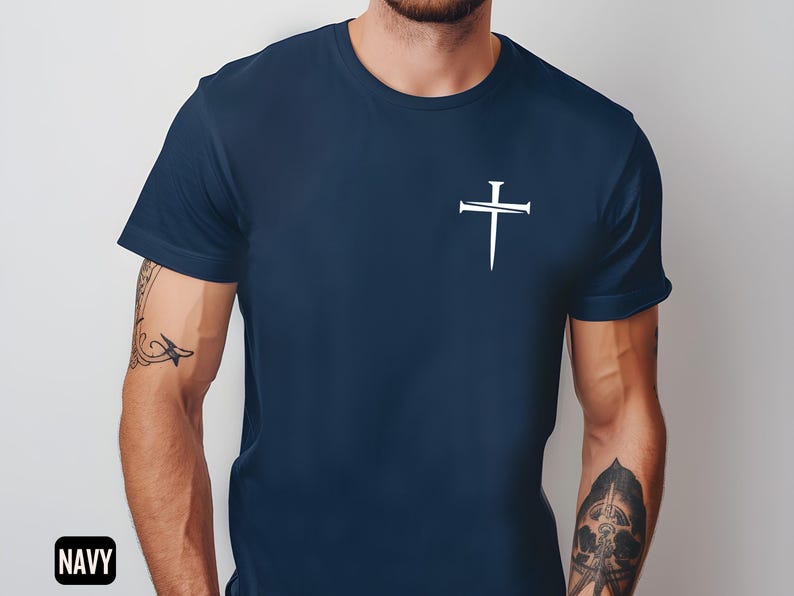 May include: A navy blue t-shirt with a white cross design featuring nails. The cross is centered on the chest of the shirt.