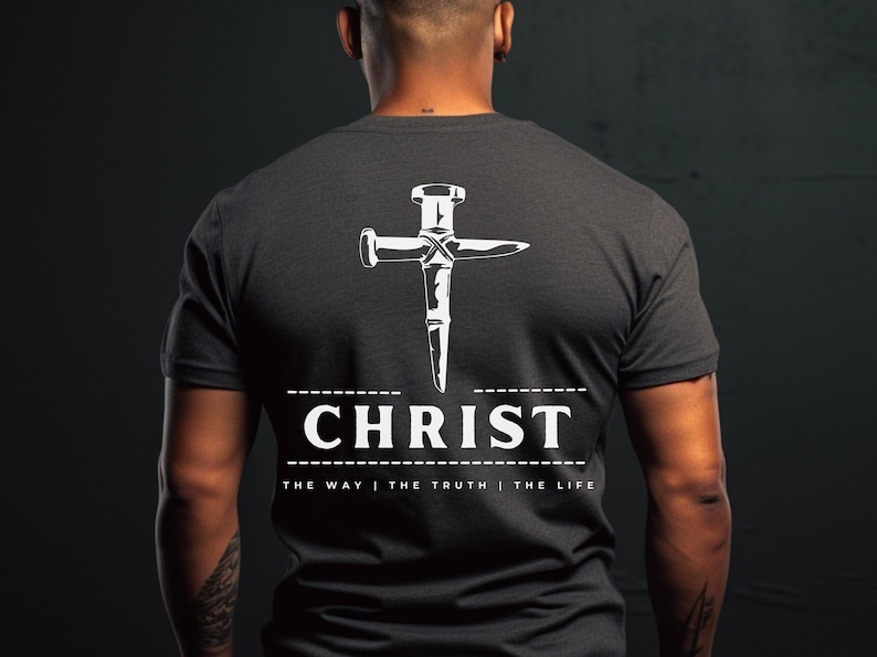 May include: A dark grey t-shirt with a white graphic of a nail hammered into a cross. The text "CHRIST" is below the cross with the phrase "THE WAY | THE TRUTH | THE LIFE" underneath.