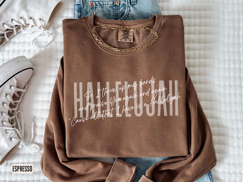 May include: A brown long-sleeve crewneck sweatshirt featuring the word HALLELUJAH in large block letters with the cursive text So I throw up my hands and praise You again and again 'Cause all that I have is a Hallelujah layered over it.