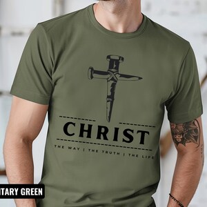May include: A military green t-shirt with a graphic of a nail hammered into a cross. The text "CHRIST THE WAY | THE TRUTH | THE LIFE" is printed below the graphic.