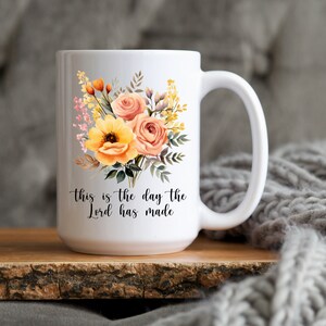 Puede incluir: Taza de cer&aacute;mica blanca con un dise&ntilde;o floral con flores amarillas y naranjas. La taza tiene una inscripci&oacute;n negra que dice "This is the day the Lord has made."