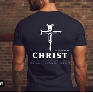 May include: Navy blue t-shirt with a white graphic of a nail hammered into a cross. The text "CHRIST" is below the cross with the phrase "THE WAY | THE TRUTH | THE LIFE" underneath.