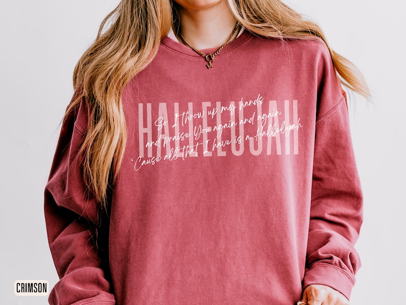 May include: A crimson crewneck sweatshirt featuring the word HALLELUJAH in large white block letters. Overlaid is the white cursive text: So I throw up my hands and praise You again and again 'Cause all that I have is a Hallelujah.