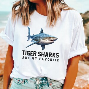 May include: White t-shirt with a graphic of a tiger shark and the text "Tiger Sharks Are My Favorite".