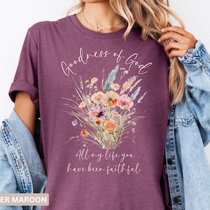 May include: Heather maroon t-shirt with a floral bouquet design. The shirt features the words "Goodness of God" and "All my life you have been faithful" in a script font. The floral arrangement includes pink, orange, and blue flowers.